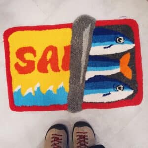 Alfombra artesanal hecha a mano con técnica tufting diseño lata de sardinas abierta en colores rojo, amarillo y azul.